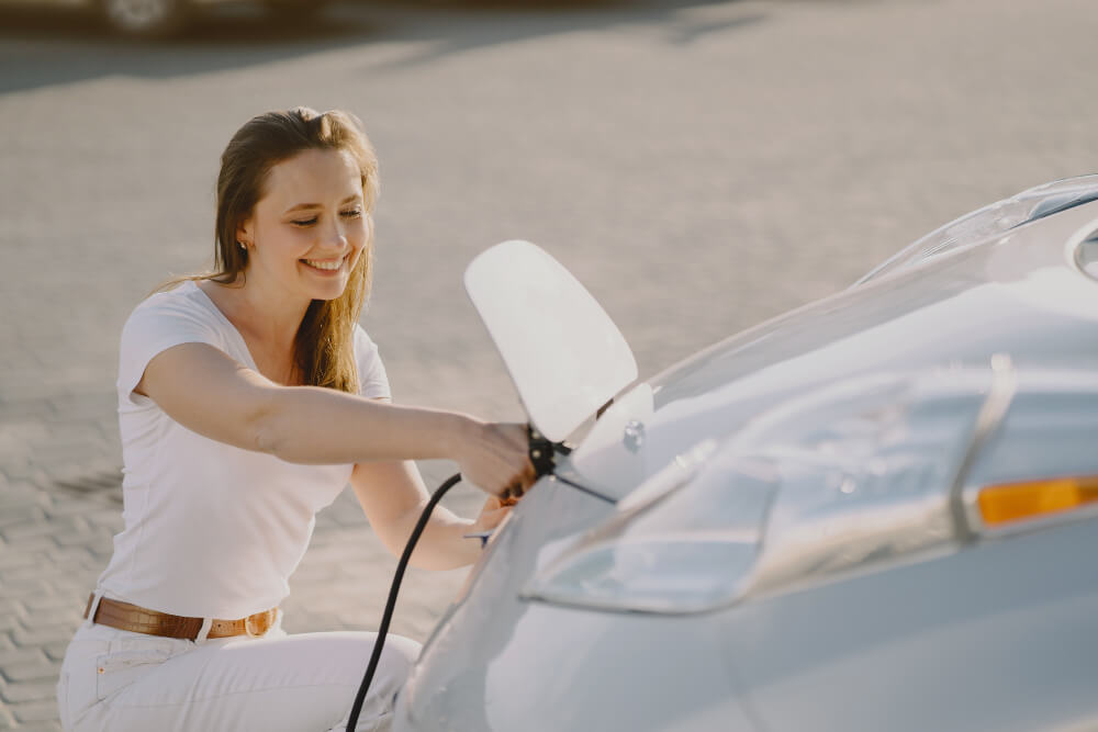 Mujer enchufando su coche eléctrico al sol, aprovechando los excedentes de la instalación fotovoltaica