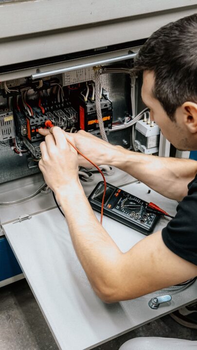 Instalador electricista midiendo con un multímetro dentro de un cuadro eléctrico abierto durante una revisión